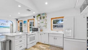 A modern kitchen with white cabinetry, a built-in oven, a microwave, and a refrigerator. There is a wooden floor and a small trash can. - Private POOL/SPA-Almost beachfront, Amazing Gulf Views, walk to Bridge St. (Bradenton Beach)