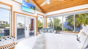 A bedroom with a large bed, a ceiling fan, and a view of palm trees and a pool. - Private POOL/SPA-Almost beachfront, Amazing Gulf Views, walk to Bridge St. (Bradenton Beach)