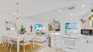 A modern kitchen with white cabinetry, a built-in oven, and a microwave. There is a dining area with a table and chairs, and a chandelier above. - Private POOL/SPA-Almost beachfront, Amazing Gulf Views, walk to Bridge St. (Bradenton Beach)