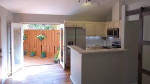 A kitchen with white cabinets, a refrigerator, a microwave, and a sink. There is a wooden door leading to a patio with potted plants. - Raleigh's famous mushroom house (Raleigh)