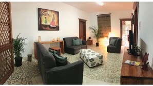 Una sala de estar con un sofá, un reposapiés y una mesa de centro. Hay un cuadro en la pared y una planta en maceta.