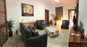 A living room with a sofa, ottoman, and a coffee table. There is a painting on the wall and a potted plant. - Spacious House (Oaxaca de Juárez)