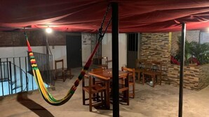 Un patio cubierto con una hamaca, una mesa de comedor de madera, sillas y un muro de ladrillo.