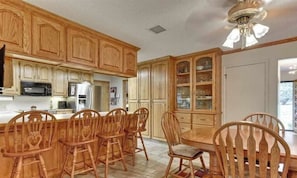 A kitchen with wooden cabinets, a dining table with chairs, a refrigerator, and a microwave.