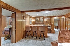 A bar area with wooden paneling, a bar counter, and three stools.