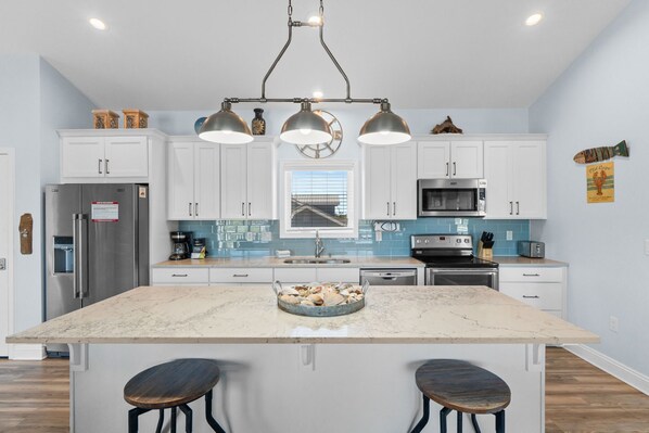 A modern kitchen with white cabinets, a large island with stools, stainless steel appliances, and a pendant light fixture. - Sunny Paws- Pet Friendly & Golf Cart (Port St. Joe)