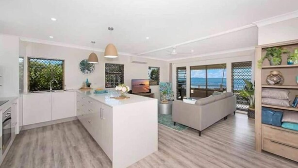 A modern kitchen with white cabinets, a central island, and a dining area with a sofa and table. - Amazing Oceanfront retreat at Saunders Beach (Saunders Beach)