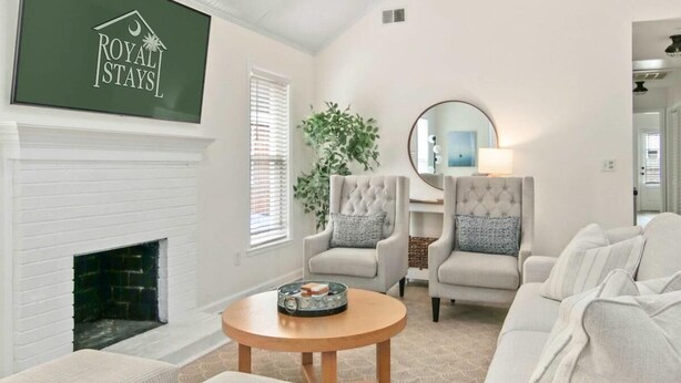 A spacious living room with a white fireplace, a large TV mounted on the wall, and a chandelier. There are two armchairs and a sofa with ottomans. - Charleston Oasis with Hot Tub, Mins to Dtwn (Mount Pleasant)