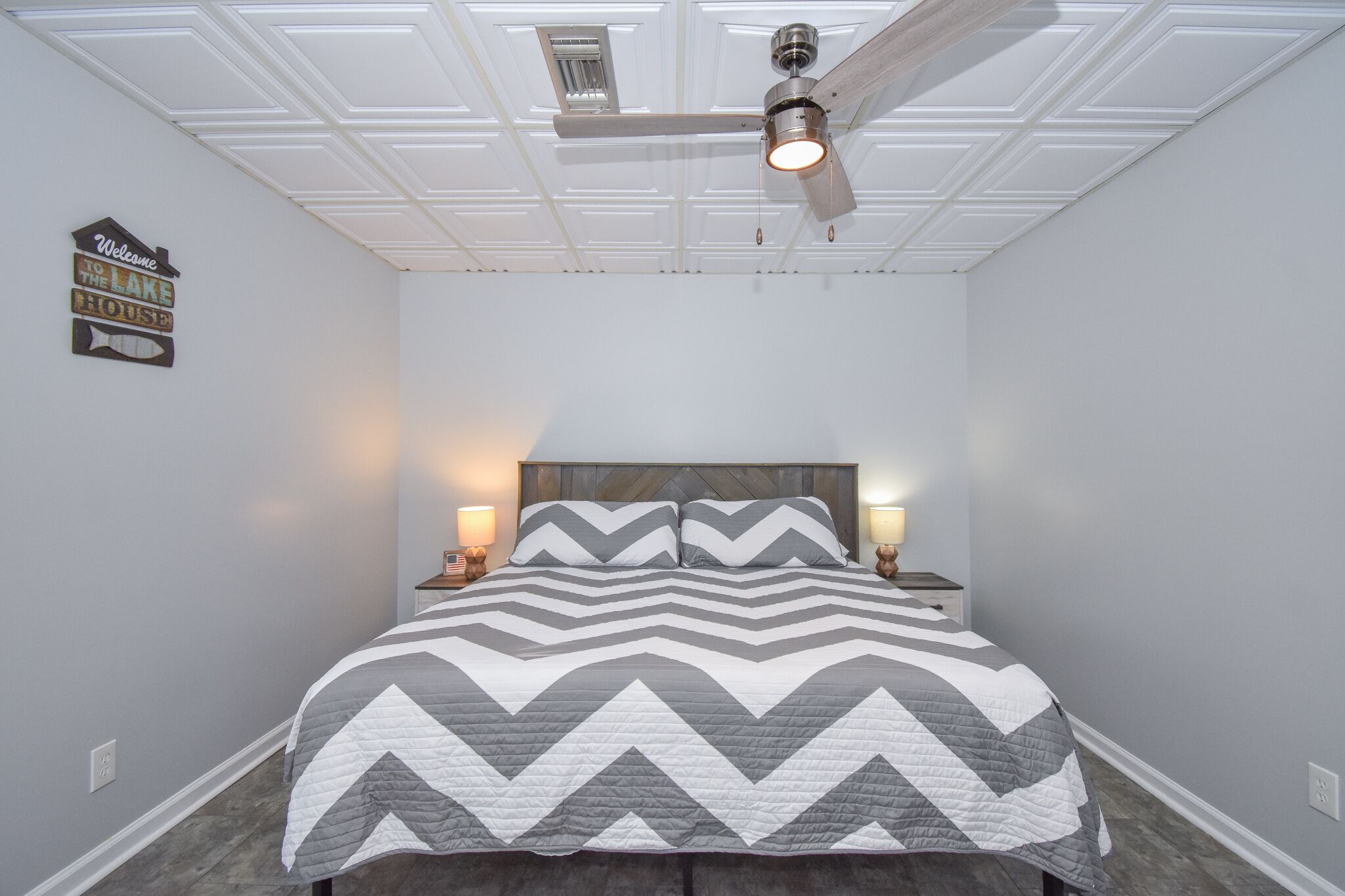 A bedroom with a bed, two bedside tables, a ceiling fan, and a wall sign.