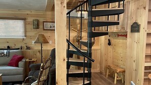 Un intérieur en bois avec un escalier en colimaçon, un canapé, un fauteuil à bascule et une petite table.