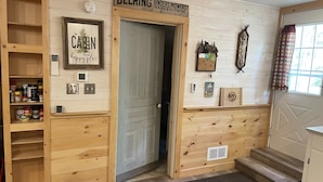 L’intérieur d’une cabane, avec une porte en bois, une étagère contenant de la nourriture pour animaux, une enseigne pour Deering Binders, Mowers, Rakes and Twine, et une affiche encadrée sur laquelle on peut lire : « Cette cabane est mon havre de paix. »