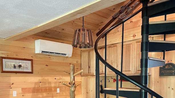 Un intérieur en bois avec un escalier en colimaçon, un fauteuil gris et un tableau encadré au mur.