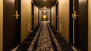 A hotel hallway with dark wood doors, numbered room signs, and a patterned carpet. - APA Hotel Kintetsu Nara Ekimae (Nara)