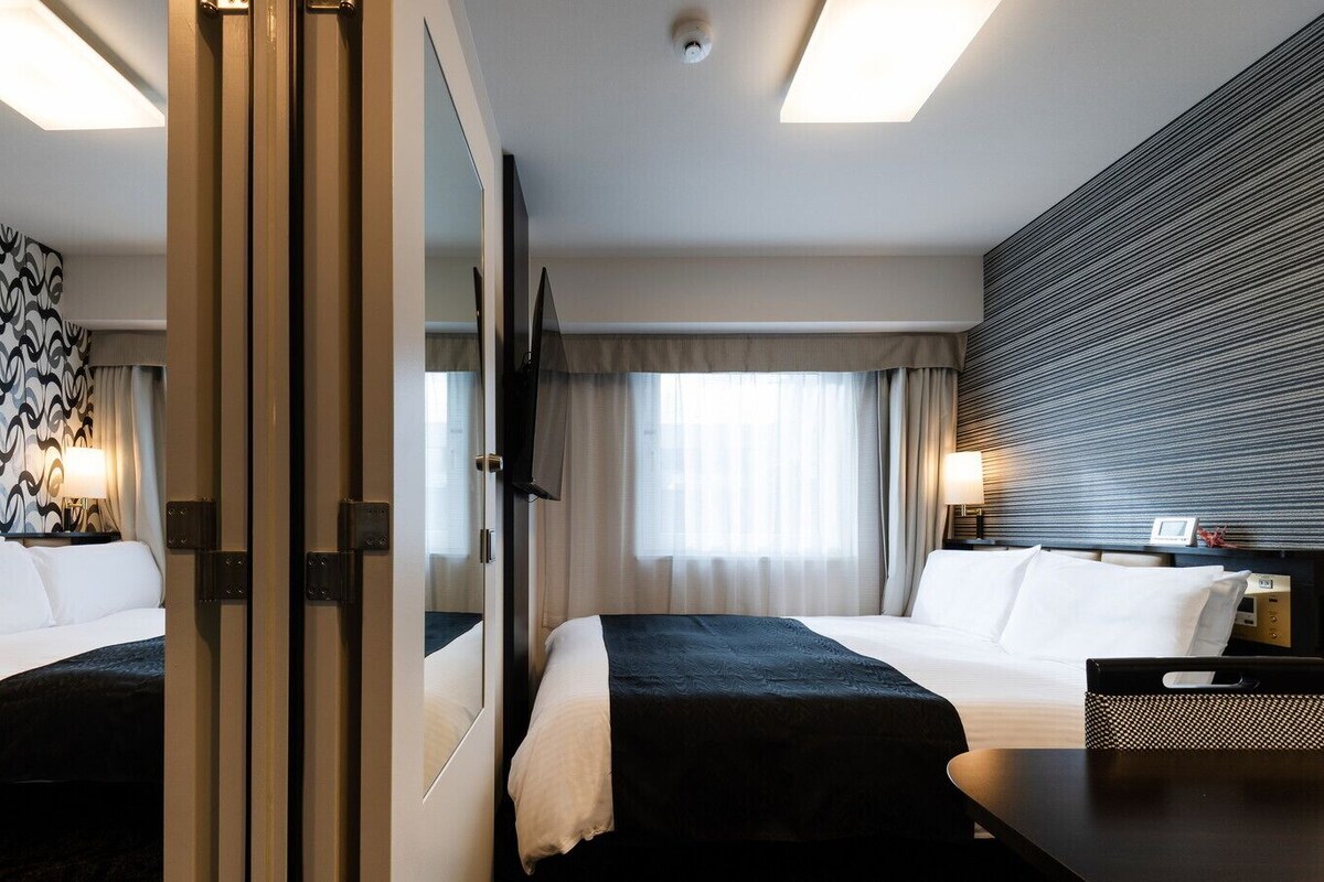 A hotel room with two beds, a large mirror, a patterned wall, and a modern light fixture.