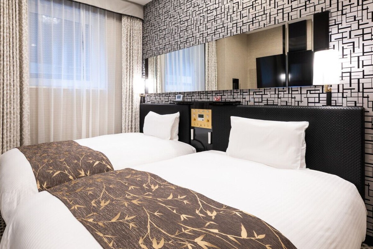 A hotel room with two beds, a minibar, a TV, and a mirror with a geometric wall design.