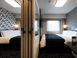 Habitación de hotel con dos camas, un espejo grande, un televisor y un papel tapiz estampado.