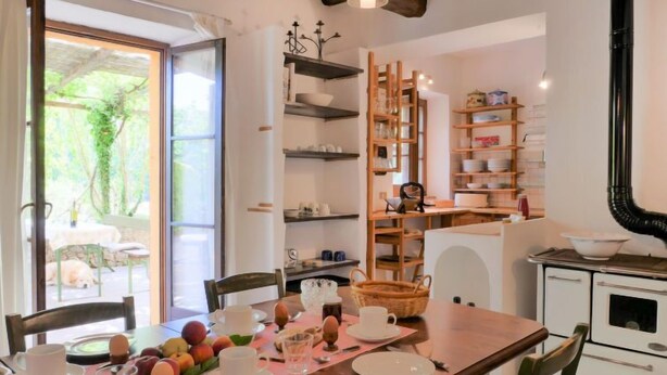 A dining area with a wooden table set for breakfast, surrounded by chairs. There is a view of a garden through an open door. - Pergola by Interhome (Boccheggiano)