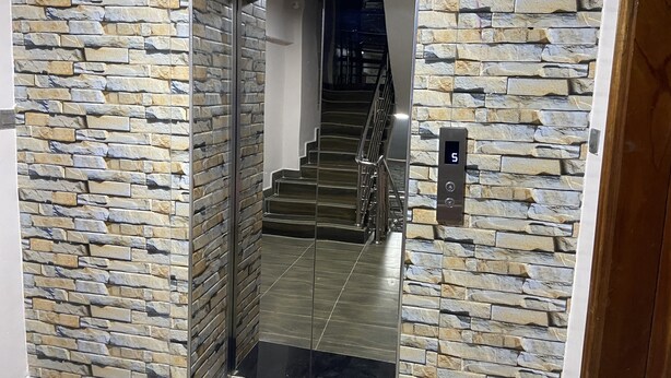 A modern elevator with a stone wall design, a metal handrail, and a digital display. - Midtown C32 Executive Suites (Nakuru)
