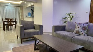 A modern living room with a grey sofa, a matching armchair, a wooden coffee table, and a striped rug. - Midtown C32 Executive Suites (Nakuru)