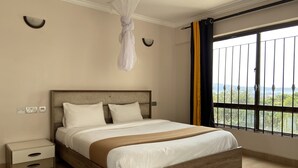 A bedroom with a bed, bedside tables, a nightstand, a window with a view, and a ceiling fan. - Midtown C32 Executive Suites (Nakuru)