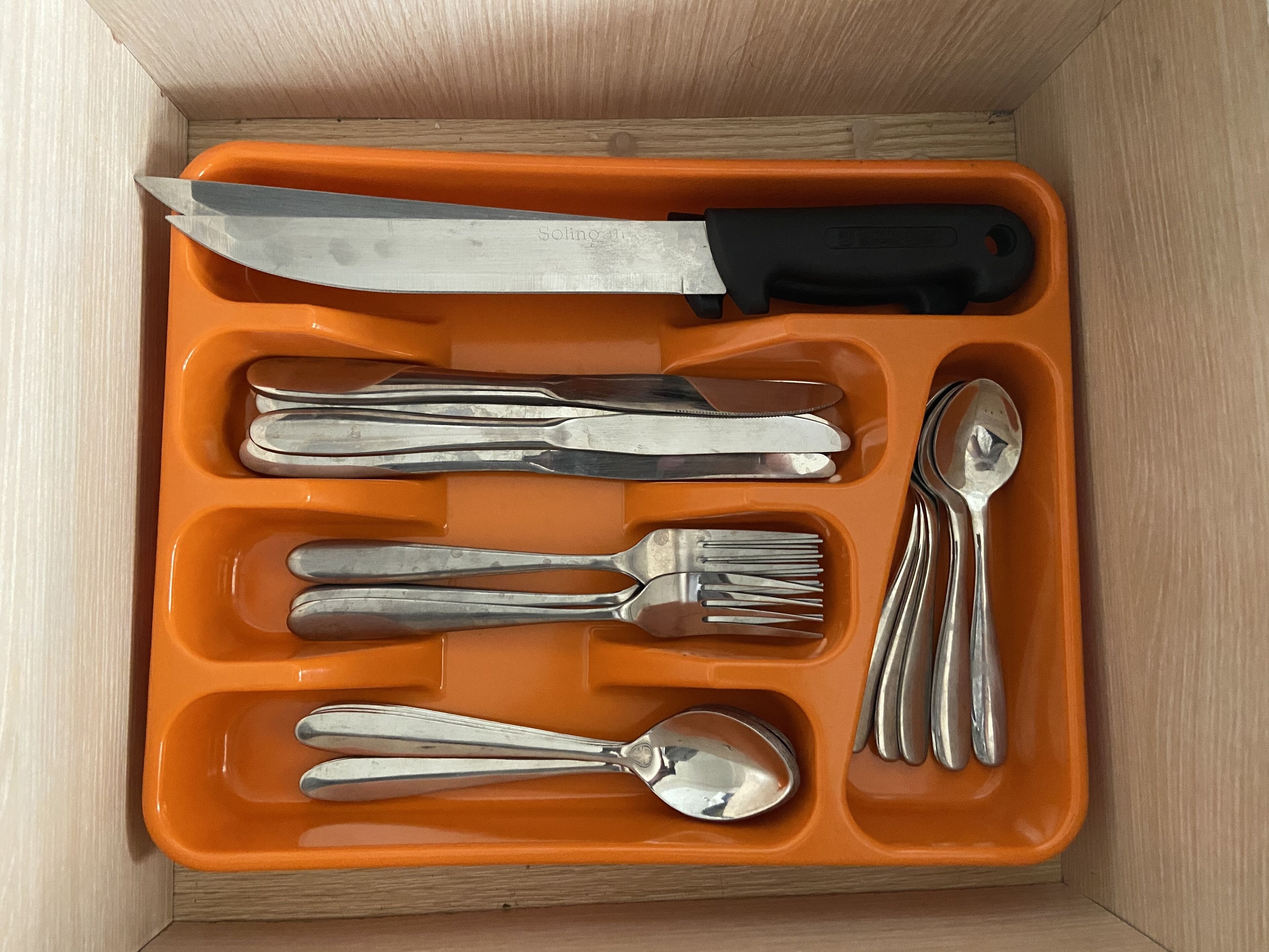 A drawer containing a knife, forks, spoons, and a spoon rest.