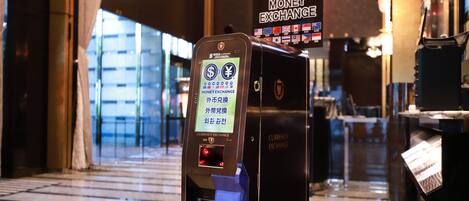 A currency exchange machine with a digital display, located in a well-lit indoor area with a glass facade in the background.