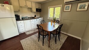 Una cocina compacta con armarios blancos, una mesa de comedor con sillas, un microondas y una estufa.