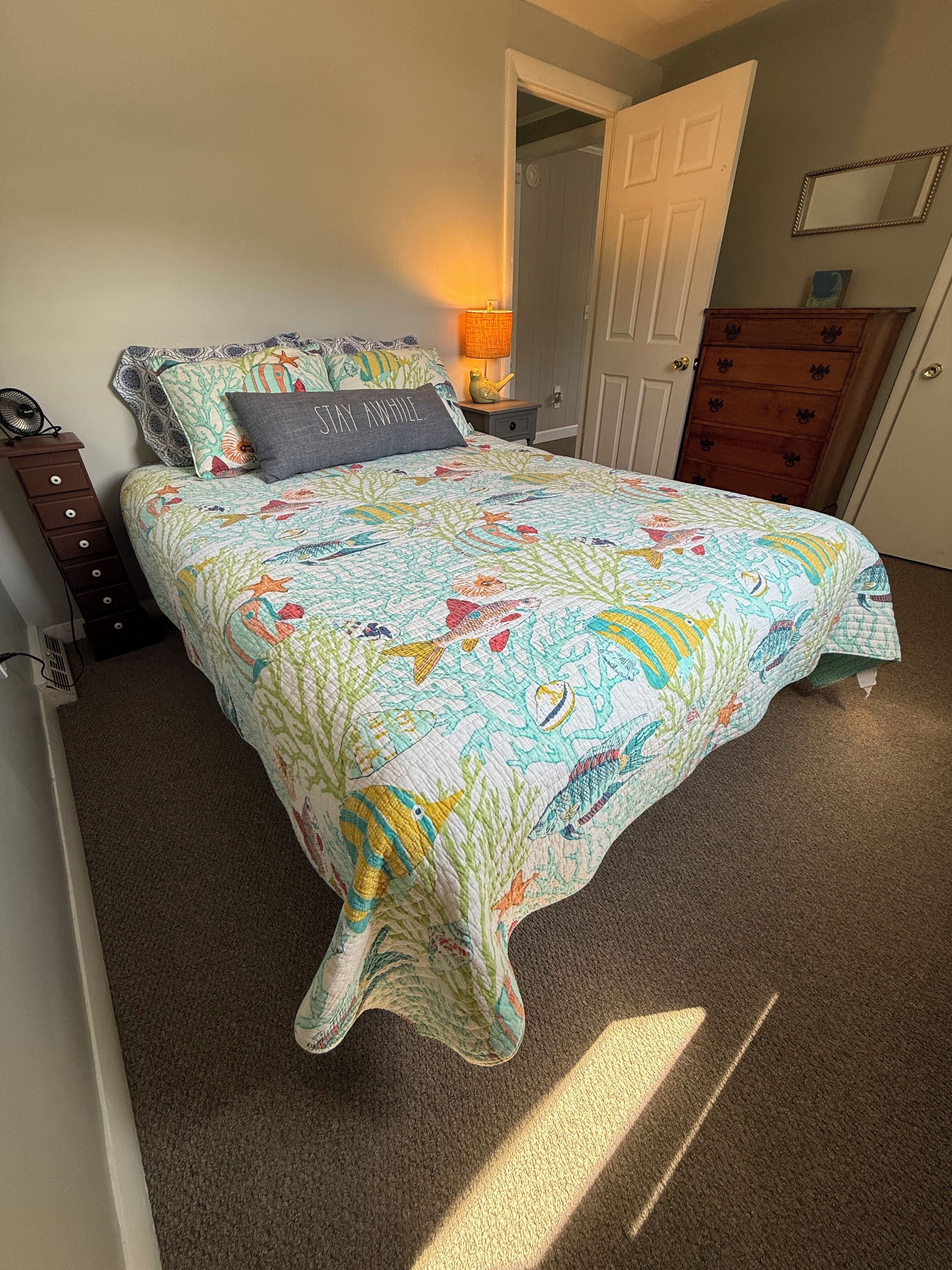 Een slaapkamer met een bed, nachtkastje, dressoir en een deur.