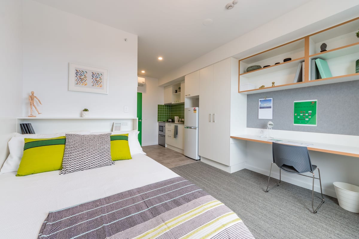 A modern hotel room with a bed, a desk, and a kitchenette.