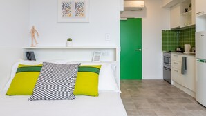 Una habitación moderna con una cama, una puerta verde y una zona de cocina.
