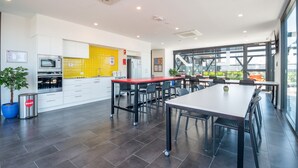 Cocina moderna con microondas, horno y salpicadero amarillo. Cuenta con un comedor con una mesa grande y sillas, y vistas al exterior a través de amplios ventanales.