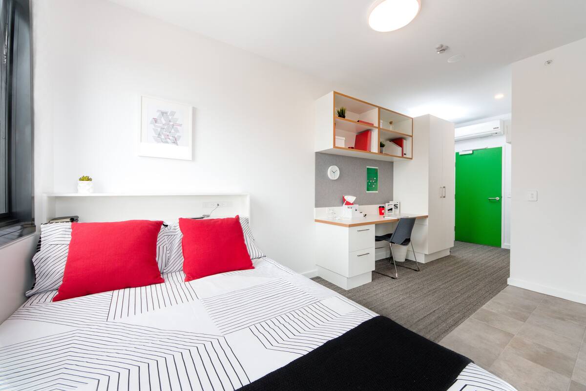 A modern hotel room with a large bed, a desk, and a green door.