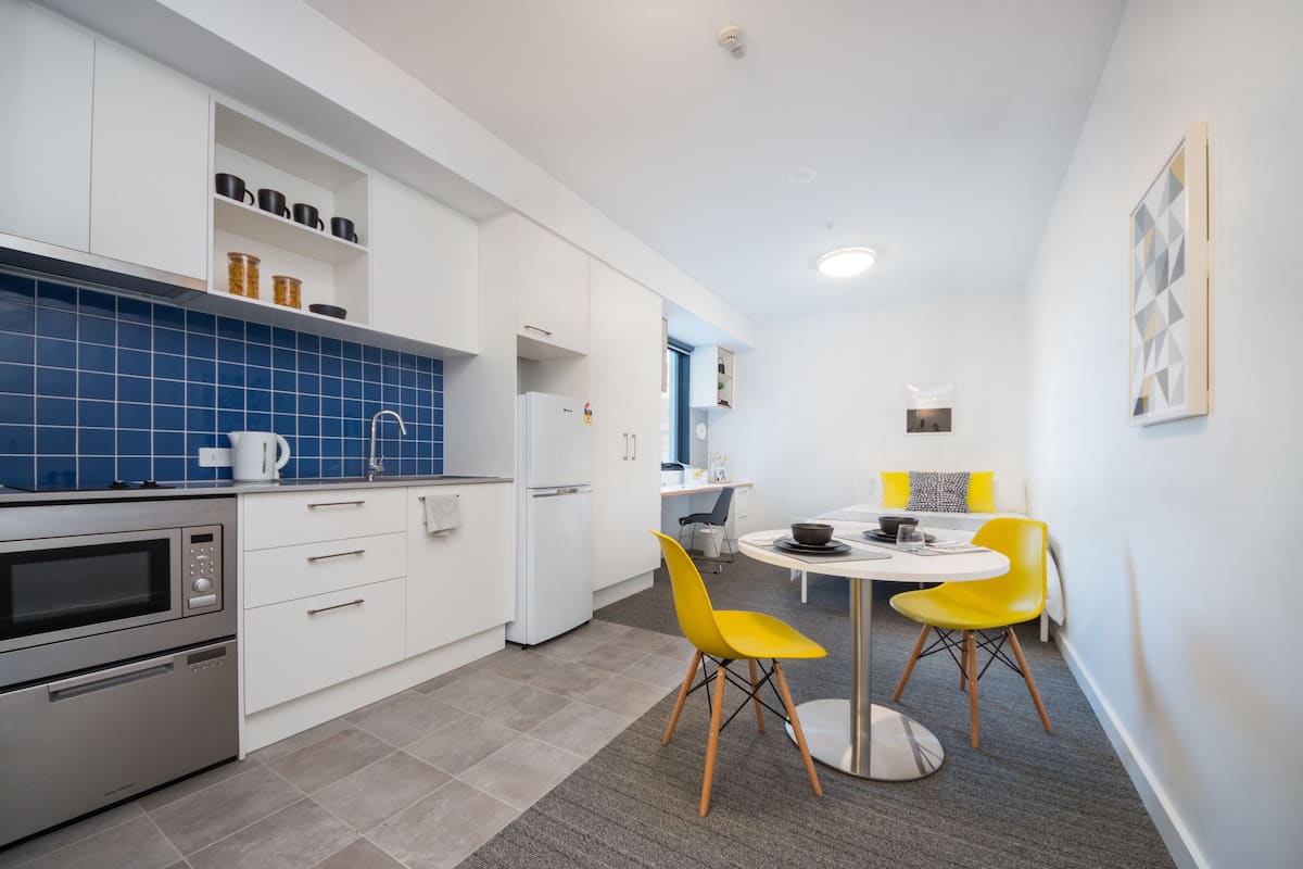 A modern kitchen with white cabinets, a blue tiled backsplash, and a dining area with a round table and yellow chairs.