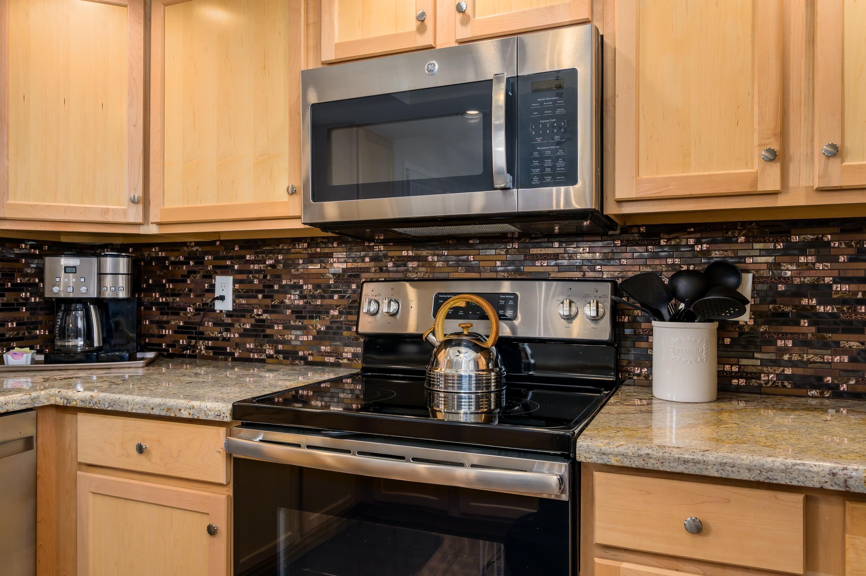 A kitchen with wooden cabinets, a stainless steel microwave, a gas stove, and a kettle.
