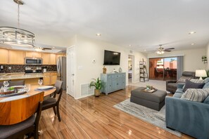 Eine moderne Küche mit Essbereich, ein Wohnzimmer mit Sofa und Fernseher, sowie ein Deckenventilator.