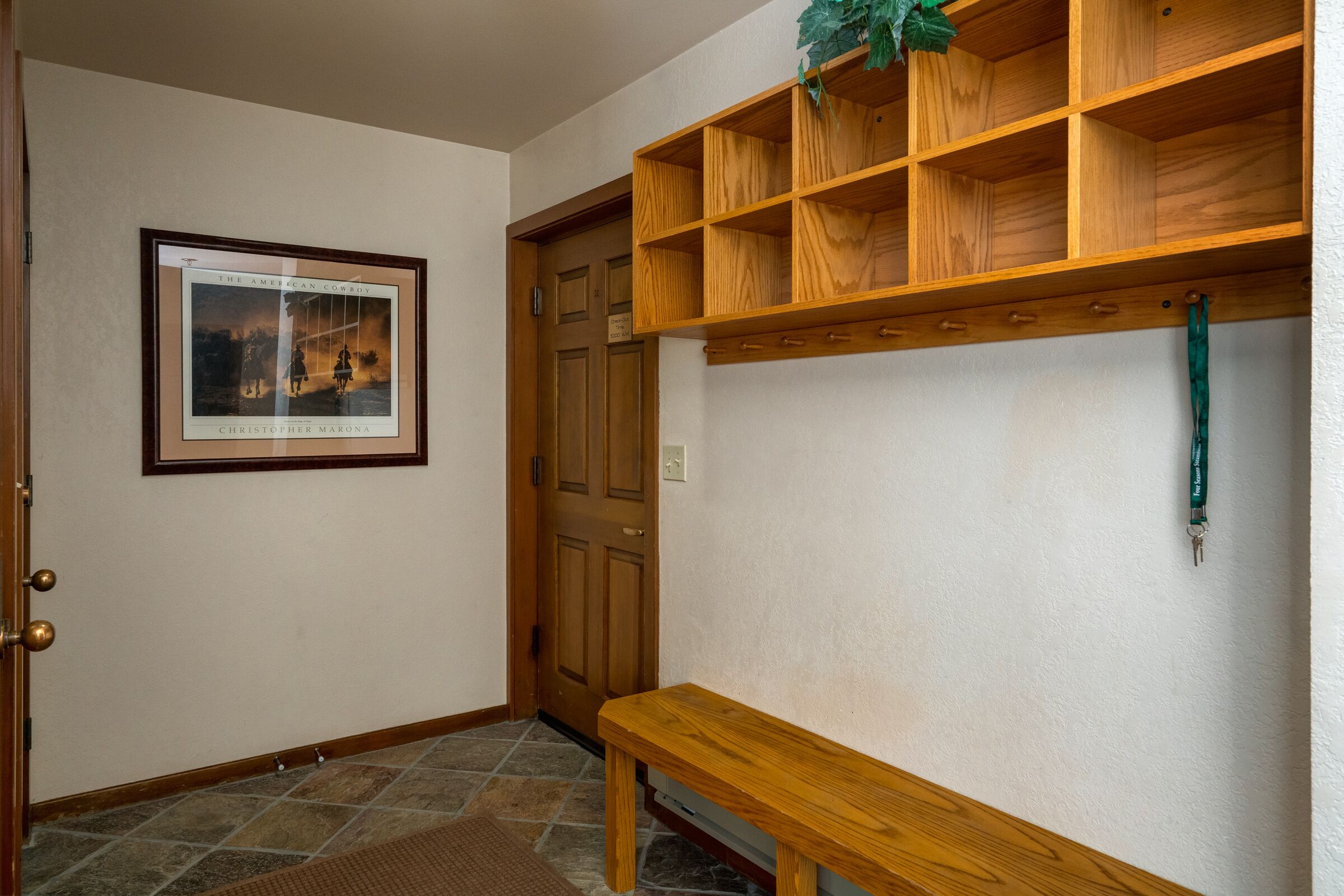 A hallway with a wooden bench, a framed picture on the wall, and a wooden shelf unit.
