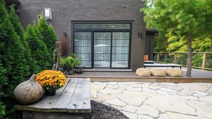 Un bâtiment moderne doté d’une terrasse en pierre, de sièges extérieurs et d’une grande fenêtre.