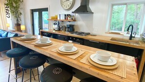 Une cuisine moderne avec un îlot central, des tabourets de bar, une horloge et une vue sur la verdure à l’extérieur.