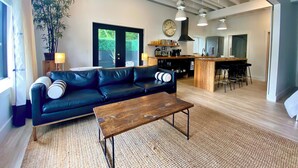 Un salon moderne avec un canapé en cuir noir, une table basse en bois et une grande fenêtre agrémentée de rideaux.