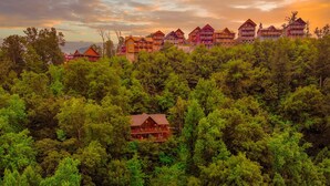 A forested area with a lodge featuring a prominent red cabin and several multi-story buildings with balconies. - Dollywood – HotTub,Theater,Pool,BBQ,Arcade & Views (Sevierville)