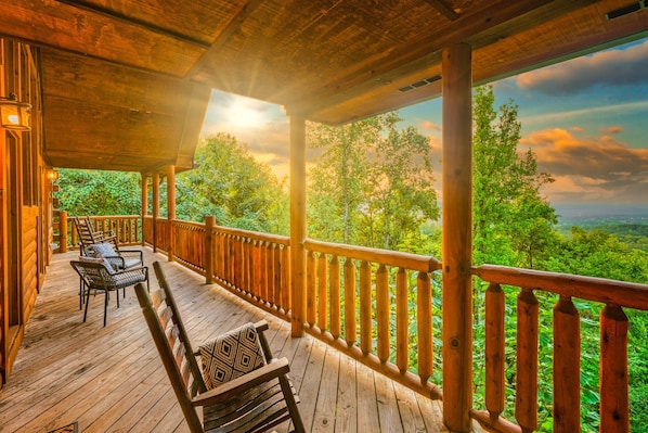 A wooden deck with chairs and a bench, overlooking a forested landscape.