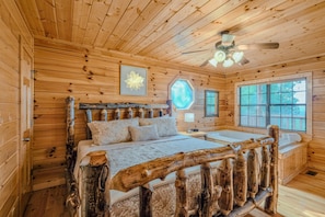 A wooden cabin bedroom with a bed, a ceiling fan, and a window.