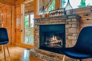 A cozy room with a stone fireplace, wooden walls, and a large window.