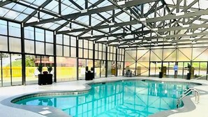 An indoor swimming pool with a glass ceiling, surrounded by a white floor and metal railings. - Dollywood – HotTub,Theater,Pool,BBQ,Arcade & Views (Sevierville)