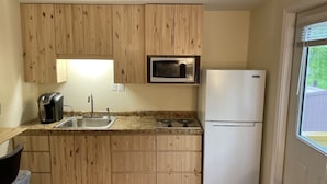 A compact kitchen with wooden cabinets, a microwave, a stove, and a refrigerator.