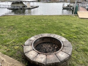 Un foyer circulaire en pierre, situé dans une zone herbeuse, avec un plan d’eau et des quais en arrière-plan.