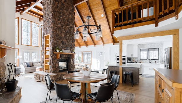 Un vaste espace de vie agrémenté d’une cheminée en pierre, de poutres apparentes en bois et d’une grande table à manger entourée de chaises.