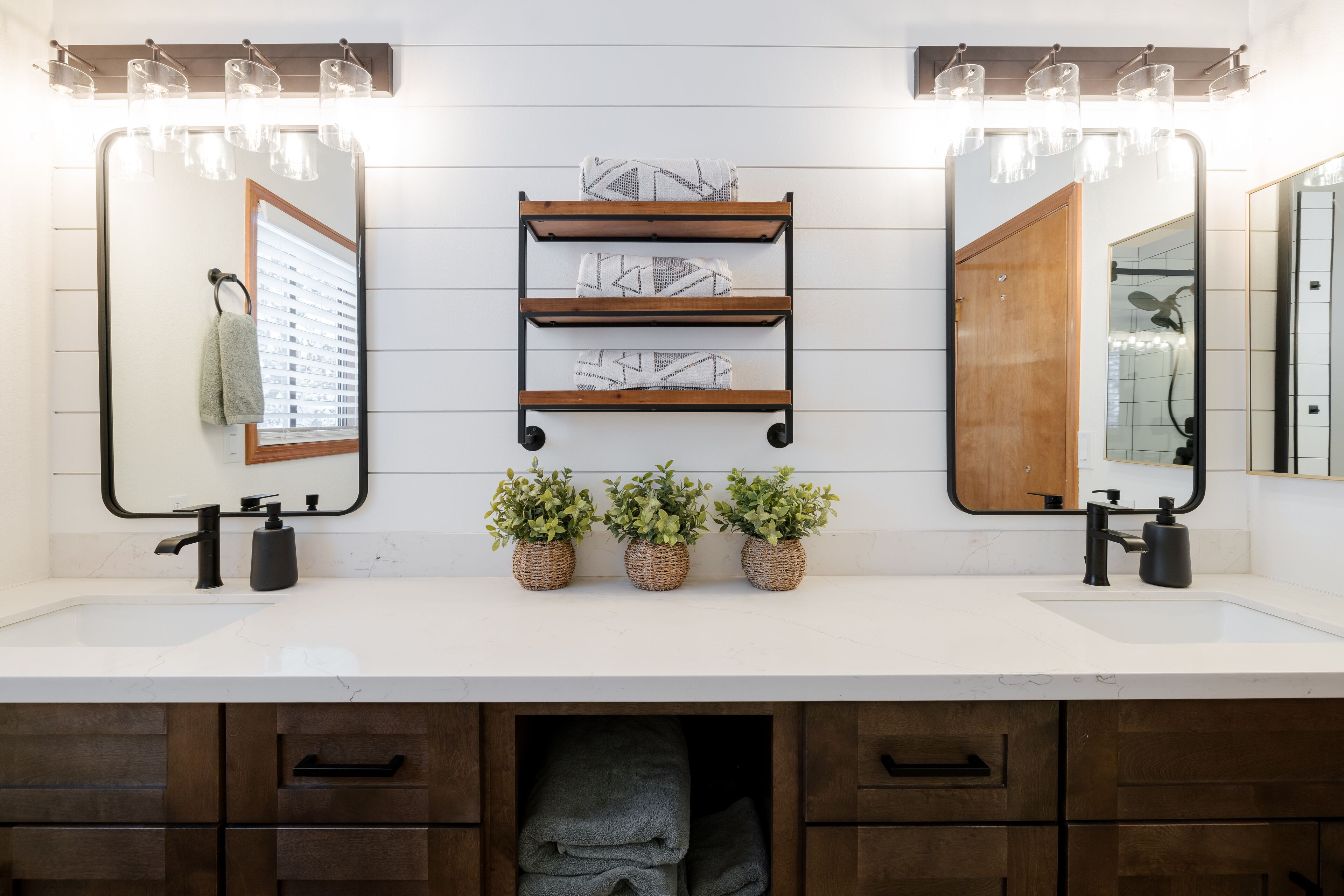 A bathroom with two mirrors, a sink, and a shelf with towels and plants.