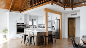Une cuisine spacieuse avec des meubles blancs, un grand îlot central doté de tabourets et un plafond en bois.