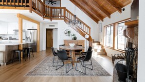 Une cuisine spacieuse avec des poutres en bois, un coin repas avec une table ronde et des chaises, et un escalier menant à un niveau supérieur.